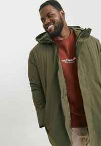 Olive green parka with a zip and snap closure, featuring a hood and front pockets, layered over a maroon sweatshirt with white text.