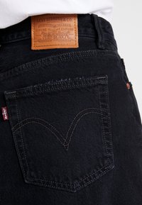 Jeans de mezclilla negra con una etiqueta de cuero marrón con logo grabado, bolsillo trasero con costura característica y etiqueta roja de Levi's.