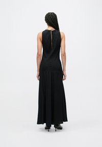 Vestido maxi preto com acabamento texturizado, design sem mangas e abertura em gota nas costas. Silhueta evasê com caimento suave.