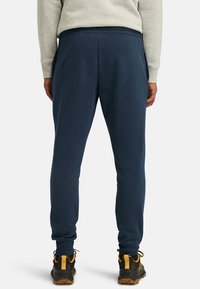 Navy blue sweatpants with a relaxed fit, elastic waistband, and side pockets, paired with black and yellow footwear.