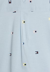 Indumento azzurro chiaro caratterizzato da un tessuto testurizzato con un sottile motivo di quadrati geometrici multicolori in rosa, giallo, nero e blu.