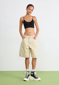 Jasne dżinsowe szorty o luźnym kroju, zestawione z czarnym topem crop i czarnymi sneakersami za kostkę. Gładka faktura i prosty design.