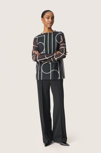 Mustat ja valkoiset kuviot sisältävä blouse geometrisilla muodoilla, yhdistettynä mustiin leveisiin housuihin ja mustiin kärkitossuihin. Liukas kangas.