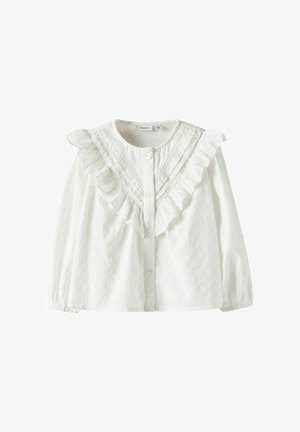 Valge puuvillane pluus, millel on volangidega krae, nööpkinnis ja tekstuuriga muster väikeste kõrguvate täppidega. Pikkade varrukatega, varrukapitsid kogutud.