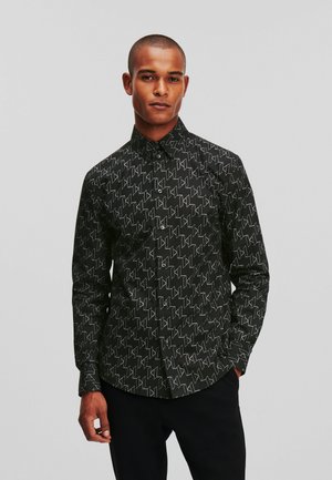 Black button-up shirt featuring a geometric white pattern, long sleeves, and a classic collar. Made from a smooth fabric with a structured fit.