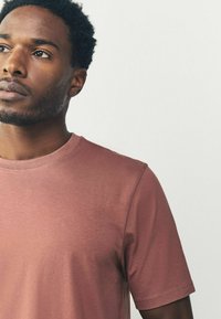 Kortærmet T-shirt i støvet lyserød farve, lavet af bomuld med en glat overflade. Har en rund halsudskæring og diskrete syninger.