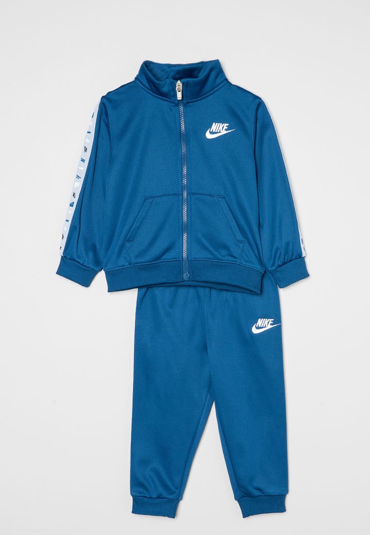 Chándal azul de Nike que consiste en una chaqueta con cremallera y cuello alto, y pantalones a juego. Presenta un logo blanco y acentos a rayas en las mangas.