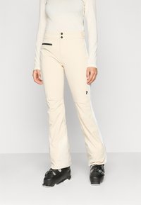 Μπεζ σκιές παντελόνια με κομψό σχέδιο, που διαθέτουν μαύρες φερμουάρ λεπτομέρειες και δύο κουμπιά στη μέση. Συνδυάζονται με μαύρες μπότες σκι.