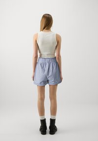 Bílý top na ramínka spojený s modro-bílými pruhovanými šortkami s vysokým pasem, které mají volánkový pas, a černými kotníkovými botami s bílými ponožkami.