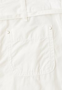 Close-up of a white fabric pocket with visible stitching and two metal rivets at the top corners.