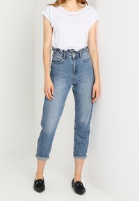 Camiseta blanca de manga corta con detalles de encaje, combinada con jeans de mezclilla azul claro de cintura alta, con los puños enrollados y mocasines negros.