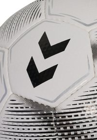 Et nærbillede af en fodbold med en glat hvid overflade, der har sorte chevron-mønstre, teksturerede paneler og grå geometriske mønstre.