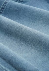 Helle blaue Denim-Stoff mit weicher Textur, der subtile Webmuster und ein glattes Finish zeigt. Mehrere Falten erzeugen Tiefe und Dimension.