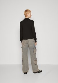 Black long-sleeve blouse, smooth fabric, paired with light gray cargo pants featuring multiple pockets and loose fit. Flat black shoes.