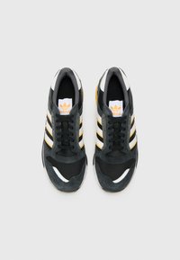Black and gray athletic shoes with a mesh upper, three white and yellow stripes, and a rubber sole. Features a padded collar and tongue.