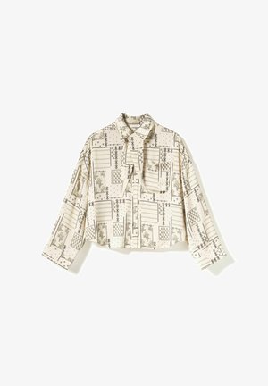 Beež pika varrukaga pluus mustade geomeetriliste ja lilliliste applikeeringutega, esitasku ning kaelaosal lipsuga detail.