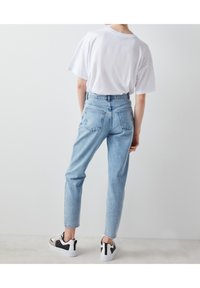 Vaaleansiniset korkeavyötäröiset farkut, joissa on kapeneva lahje ja takataskut. Yhdistetty löysästi istuvaan valkoiseen t-paitaan ja musta-valkoisiin lenkkareihin.