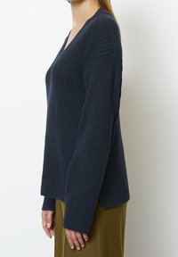 Pull côtelé bleu marine avec un col en V, manches longues et épaules tombantes. Présente un tricot texturé et une coupe décontractée.