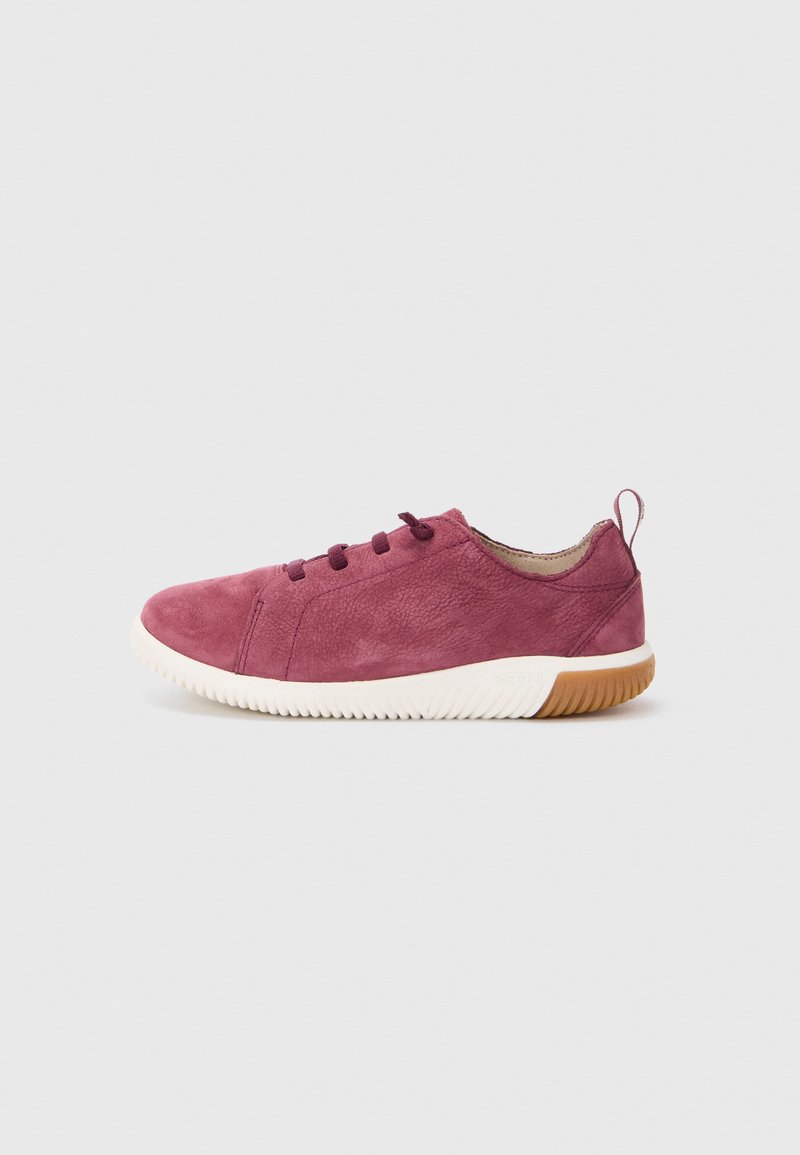 Burgundowe zamszowe sneakersy z białą gumową podeszwą, okrągłym noskiem, pięcioma oczkami i małym tylnym uchwytem dla łatwego zakładania. Teksturowana cholewka dodaje wymiaru.