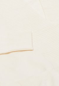 Cremefarbener Pullover mit geripptem Muster an den Ärmeln und am Körper, einer glatten, weichen Oberfläche und schräg angeordneten Designelementen.