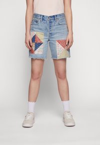 Denim shorts with frayed hem, featuring patchwork designs in red, blue, floral, and golden textures on side pockets.