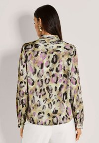 Woman with long dark hair wears a satin leopard print blouse with purple accents and gold hoop earrings, facing away from camera.