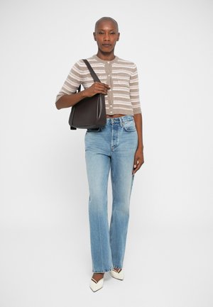 Brunstribet cardigan med korte ærmer, parret med lyseblå flagrende jeans. Sort skuldertaske, hvide spidse flade sko. Simpelt baggrund.