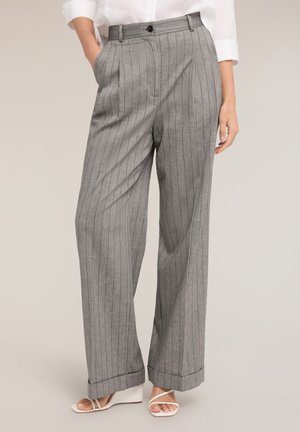 Femme portant un pantalon gris à fines rayures taille haute, à jambes larges avec revers, associé à des sandales compensées blanches à brides et une chemise blanche rentrée.