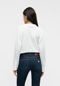 Λευκό πουκάμισο με μακριά μανίκια και γιακά, συνδυασμένο με τζιν σκούρου μπλε χρώματος που διαθέτει πίσω τσέπες και δερμάτινο λογότυπο στη ζώνη μέσης.