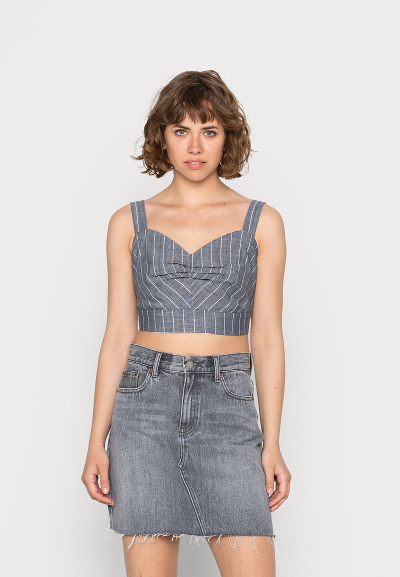 Top cropped azul e branco com riscas, de decote coração e alças largas, combinado com uma saia de ganga cinza desbotada com bainha desfiada.