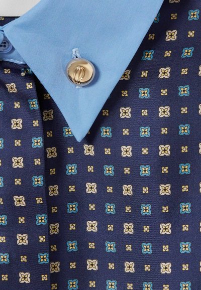 Tela con estampado navy que presenta un diseño geométrico en blanco, azul y amarillo. Cuello corto en azul claro con un botón dorado.