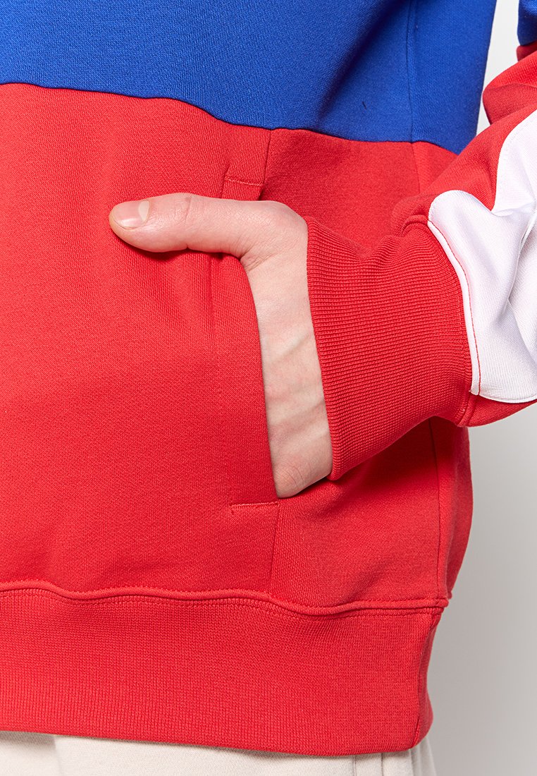 Felpa color-block con sezioni blu, rosse e bianche. Tessuto morbido con polsini a coste e una tasca frontale nella sezione inferiore rossa.