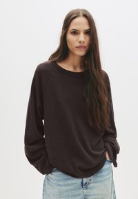 Temno sivo, dolg rokav majica z čolnasto izrezom in sproščenim krojem; v kombinaciji s svetlo modrimi jeans hlačami. Mehka tekstura in minimalističen dizajn.