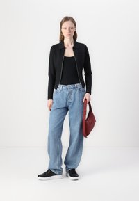Black fitted jacket with a zip closure, paired with light blue wide-leg jeans, black sneakers, and a red handbag. Smooth fabric, casual style.