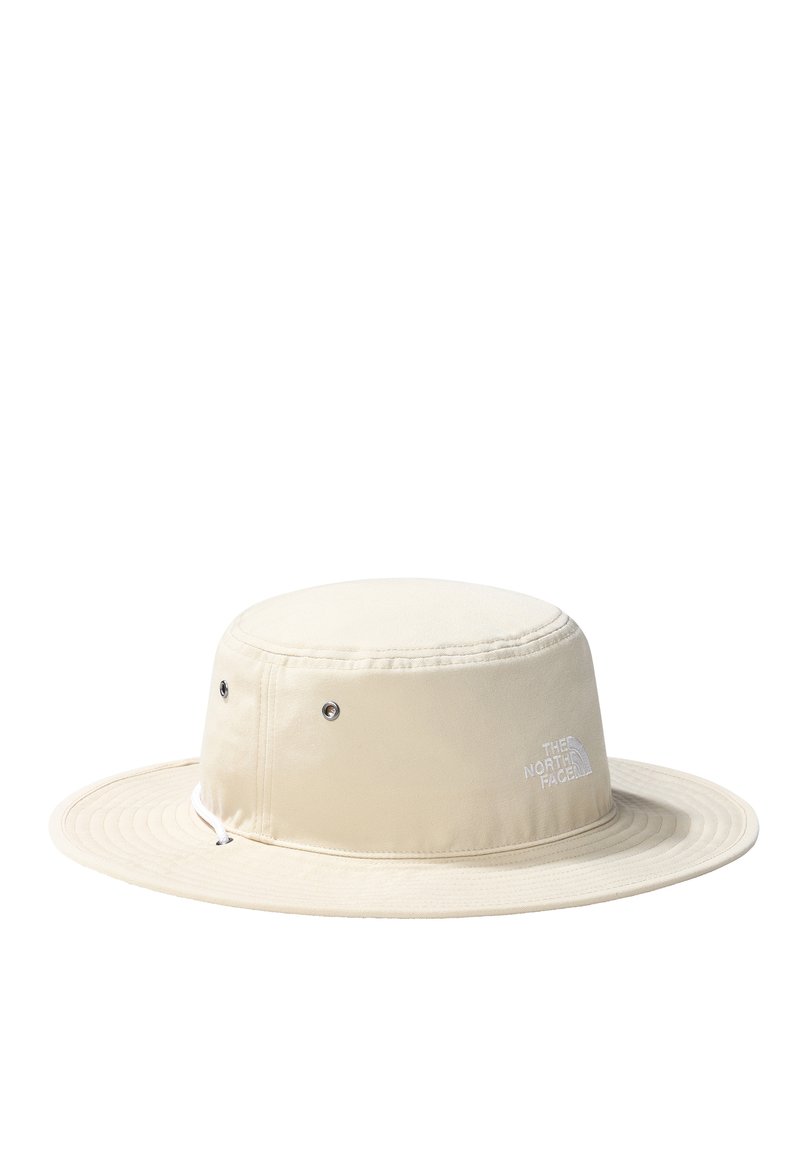 Beżowy kapelusz typu bucket na zewnątrz z szerokim rondem, wykonany z lekkiego materiału. Posiada otwory wentylacyjne oraz logo z boku.