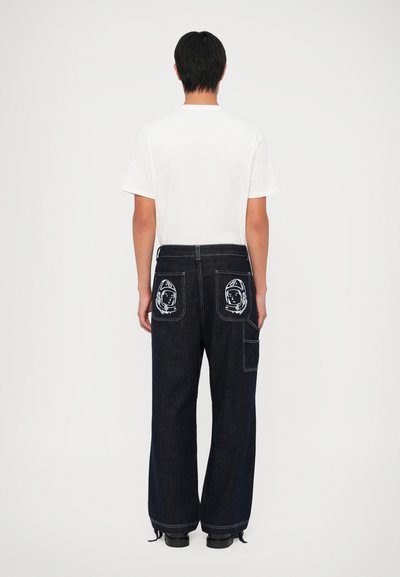 Temno modre široke jeans hlače z dvema okrasnima astronautskima nalepkama na zadnjih žepih. V kombinaciji z enostavno belo majico in črnimi čevlji.