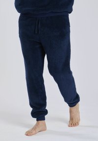 Navyblaue Fleece-Jogginghosen aus einem weichen, strukturierten Stoff mit elastischen Bündchen und einem Kordelzugbund. Ein Fuß barfuß auf einem weißen Hintergrund.