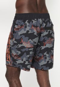 Juodos ir pilkos camo maudymosi šortai su oranžiniais ryklių grafikos motyvais, elastinga juosmens juosta, šoninės kišenės ir lengvas, tekstūruotas audinys.