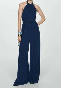 Námořnická halter overal s nařaseným pasem, širokými nohavicemi a hladkým povrchem. Doplňky zahrnují vzorovaný šátek a náramky.