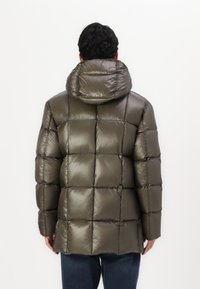 Doudoune olive verte avec un design matelassé. Dotée d'une capuche et d'une texture brillante et lisse. Coutures visibles et coupe droite.