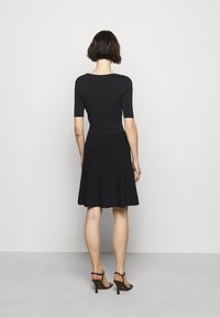 Robe noire avec un corsage ajusté, des manches courtes et une jupe fluide plissée. Conçue dans une texture côtelée, finie par un ourlet festonné.