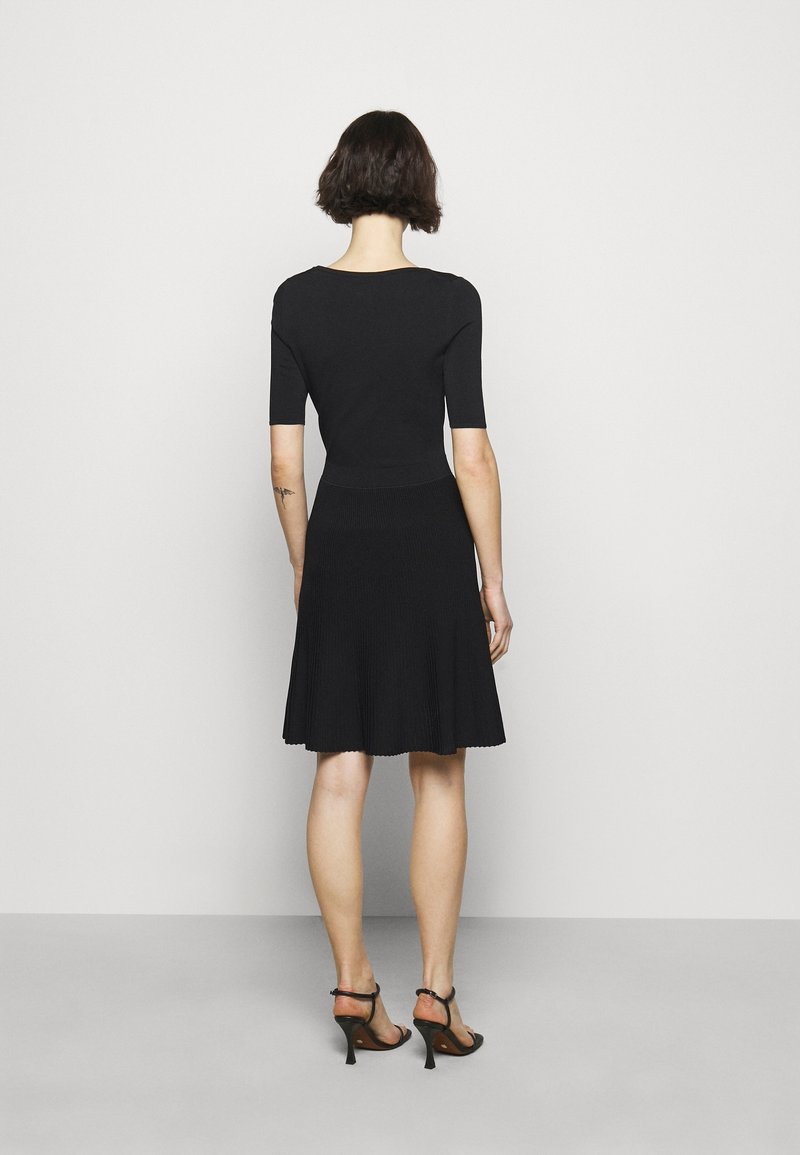 Robe noire avec un corsage ajusté, des manches courtes et une jupe fluide plissée. Conçue dans une texture côtelée, finie par un ourlet festonné.