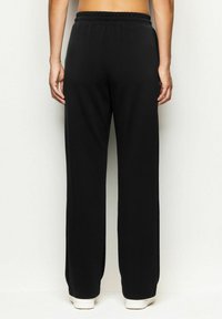 Pantaloni neri a gamba larga con vita elastica, texture liscia e design alla caviglia; dettagli minimi e senza tasche visibili.