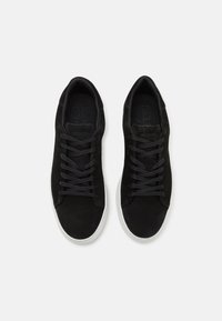 Czarne zamszowe sneakersy z płaskimi czarnymi sznurówkami, o zaokrąglonym kształcie noska i białej gumowej podeszwie. Minimalistyczny design, bez widocznych logo czy wzorów.