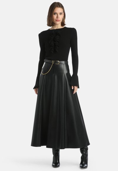 Pulover negru din tricot cu o textură ondulată la gât, asortat cu o fustă lungă din piele neagră și cizme negre cu toc ankle.