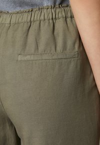 Olijfgroen, lichtgewicht broek van stof met een elastische tailleband en een enkele achterzak met een vlakke opening. Glad textuur.