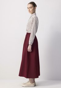 Blouse à rayures à manches longues en crème et marron, associée à une jupe bourgogne longueur cheville. Le modèle porte des baskets beiges.