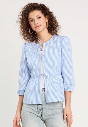 Light blue and white striped blouse with a round neck, puff sleeves, front tie closure, and peplum hem. Worn over a white top.