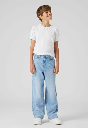 Weißes T-Shirt mit kurzen Ärmeln, hellblaue weit geschnittene Jeans und weiße Sneaker. Das Outfit zeichnet sich durch eine lockere Passform und ein lässiges Design aus.
