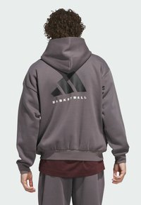 Siva dukserica s kapuljačom koja ima veliki crni trouglasti logo i reč "BASKETBALL" u belom tekstu. Rebrast rub i manžetne. Mekani materijal.